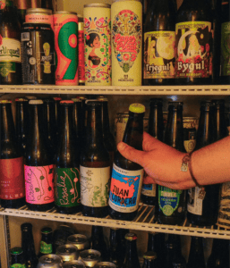 Cerveza artesanal en botella, exhibida en estantería con otras bebidas en tienda especializada.
